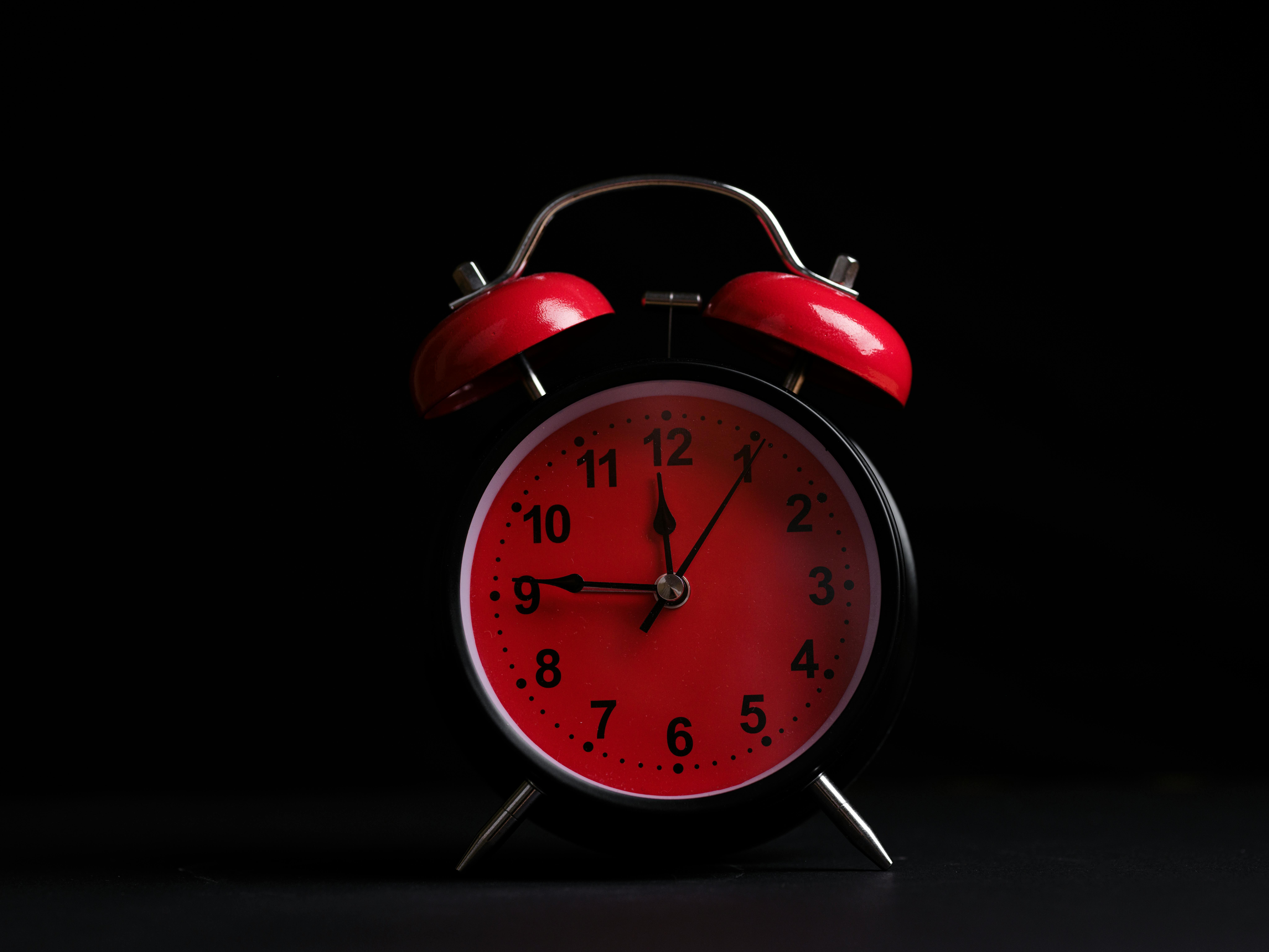 Retro analog alarm clock with red face and bells, showcasing classic design on a black backdrop.